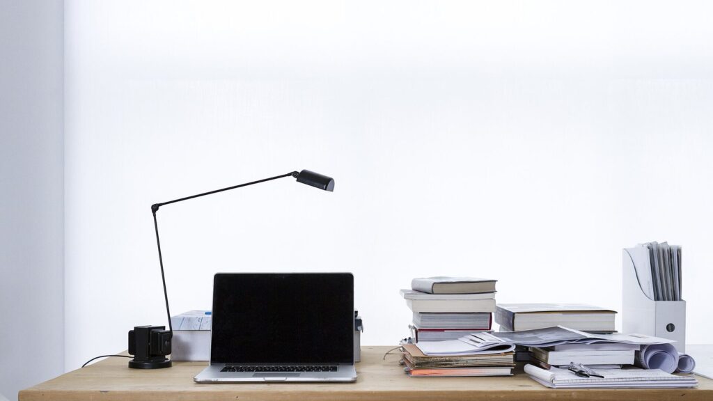 Scrivania di studio professionale con portatile, lampada e pile di libri e documenti