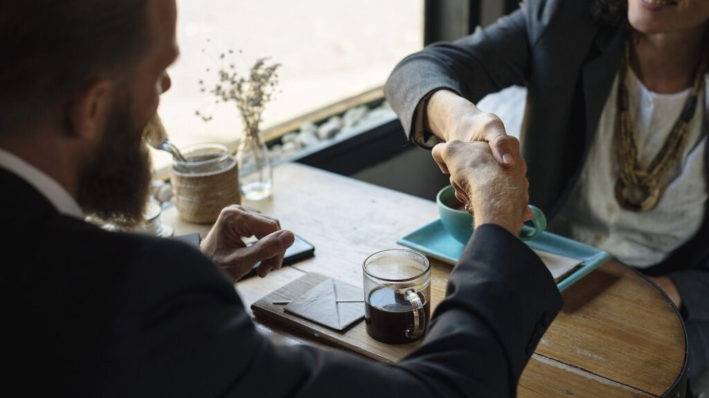 Stretta di mano tra consulente e cliente a un tavolo di caffè, a conclusione di un incontro